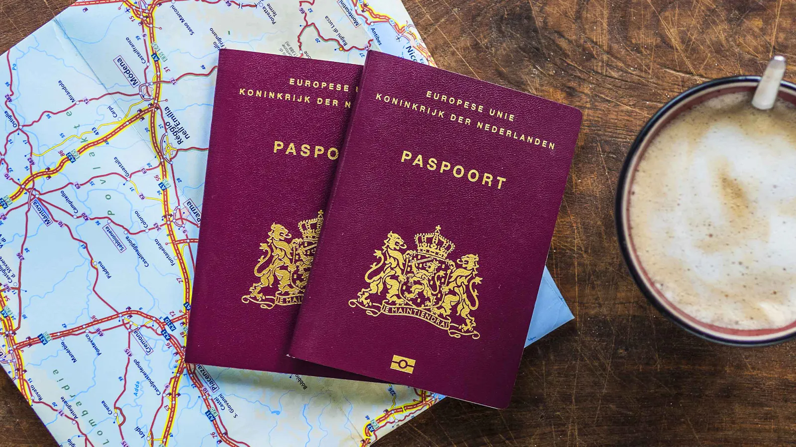 2 paspoorten liggen op tafel met een landkaart en een kop koffie er naast