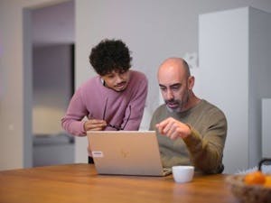 Staande man en zittende man kijken naar een laptop op tafel