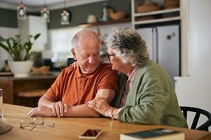 Senior vrouw troost senior man zittend aan tafel.