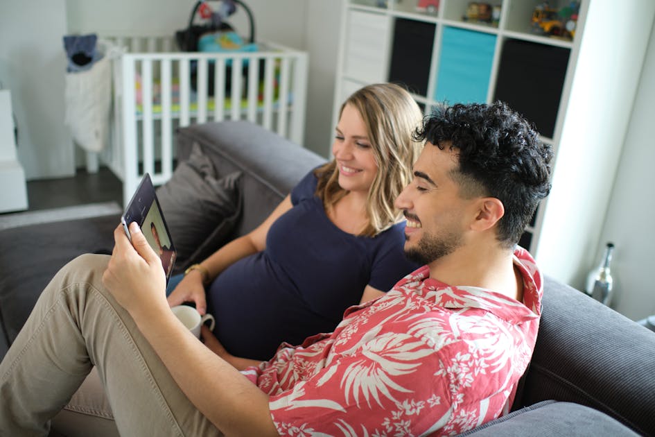 Zwangere vrouw en man zitten op de bank en kijken naar een tablet