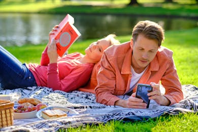 Vrouw leest boek en man kijkt op mobiel