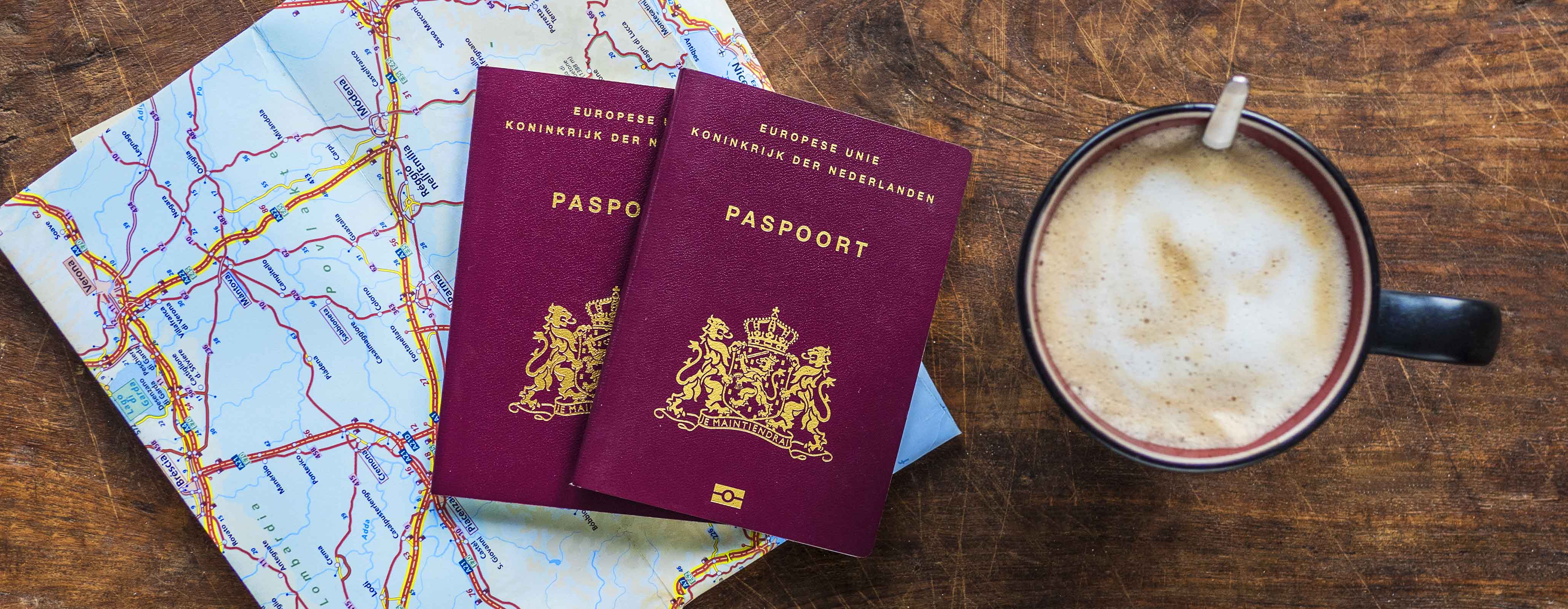 2 paspoorten liggen op tafel met een landkaart en een kop koffie er naast