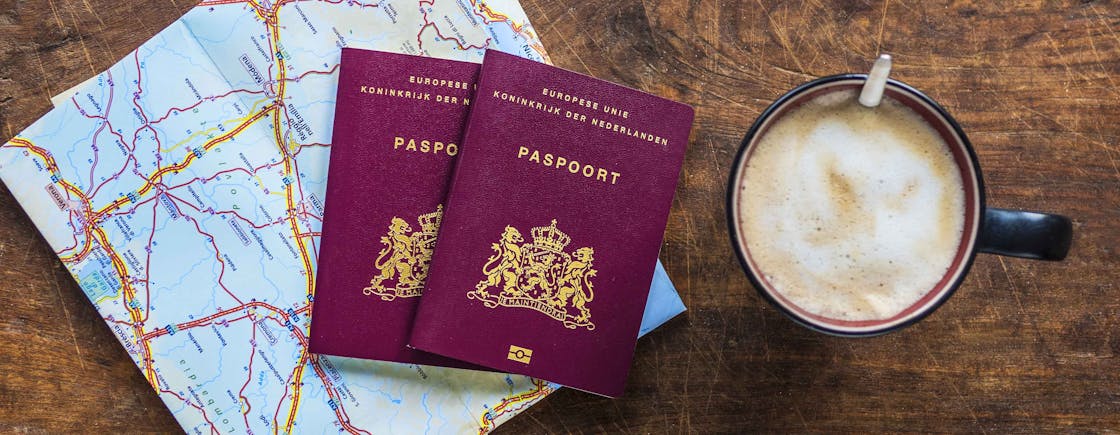 2 paspoorten liggen op tafel met een landkaart en een kop koffie er naast