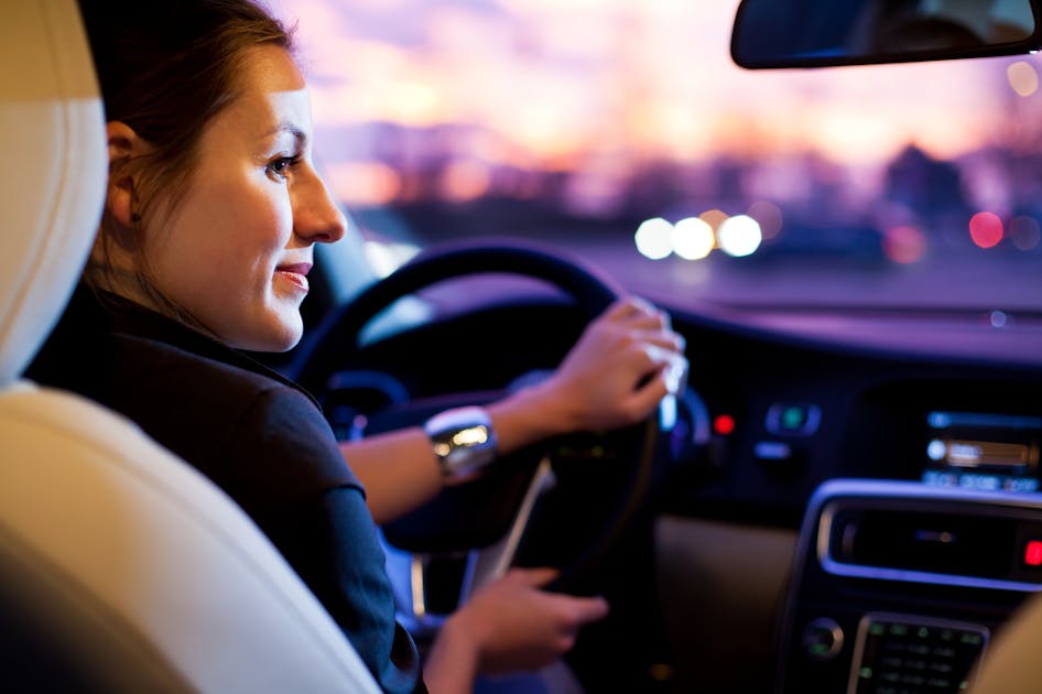 Vrouw in auto die in het schemer rijdt en licht van koplampen van andere auto’s ziet.