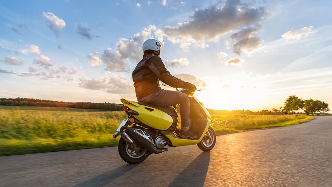 Persoon op gele scooter tijdens zonsopkomst zonder scooterpech