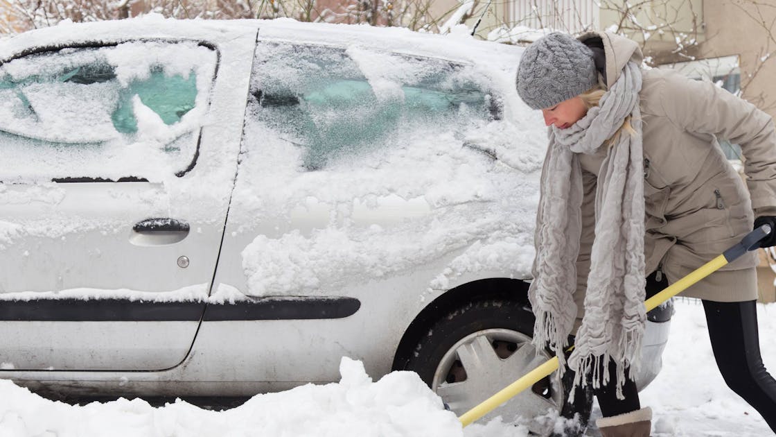 Vrouw schept sneeuw bij auto weg