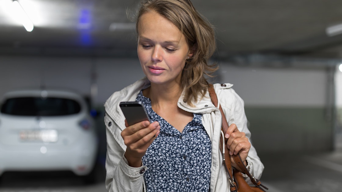 Vrouw checkt smartphone in pakeergarage met elektrische auto geparkeerd