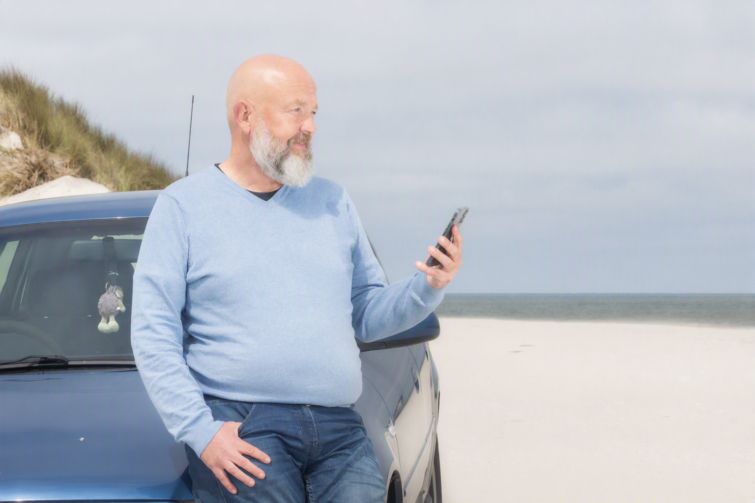 Hans staat op het strand met een telefoon in zijn hand