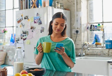  Vrouw met koffie en smartphone in de keuken