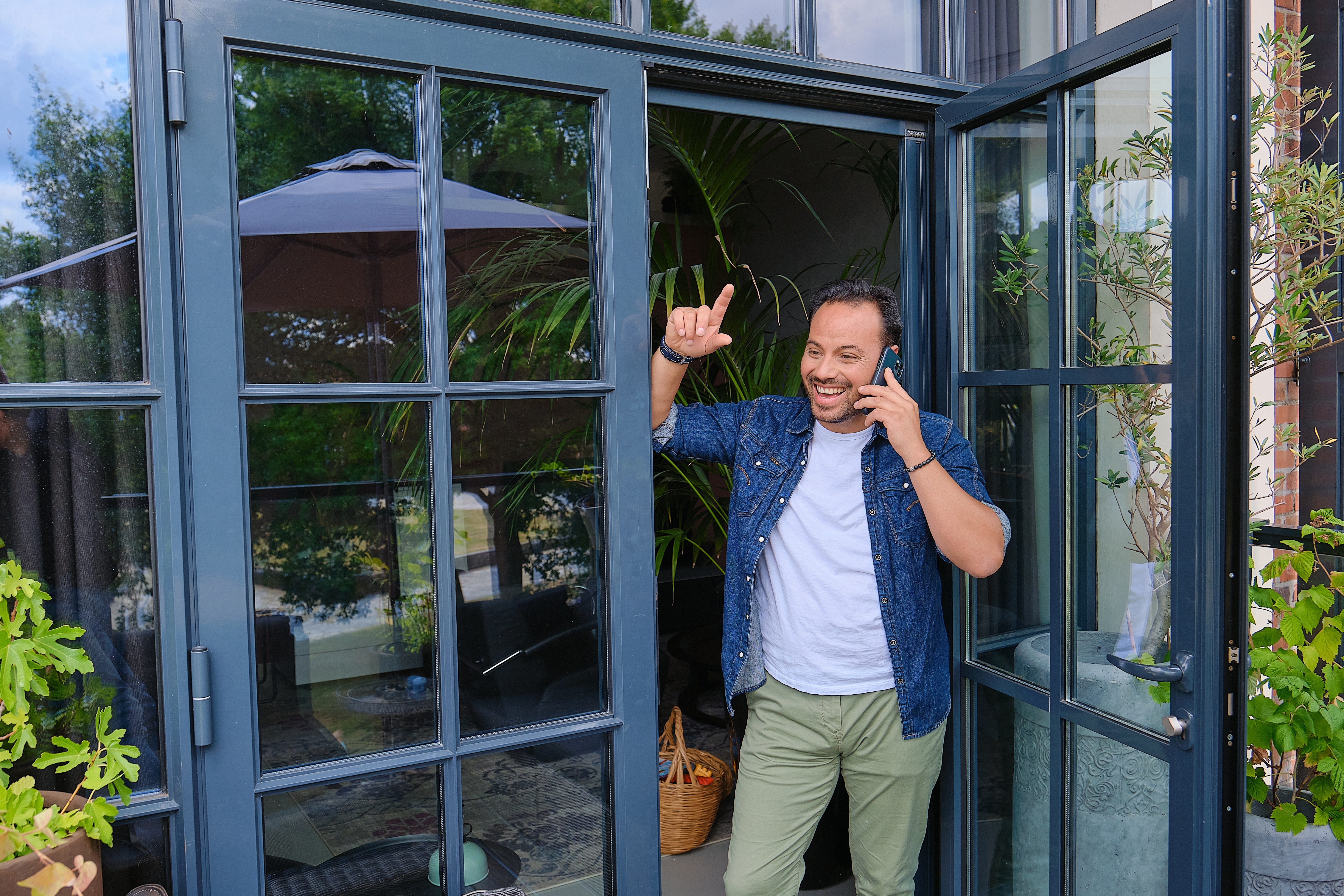  Een man staat in een deuropening, belt en maakt een enthousiaste handbeweging.