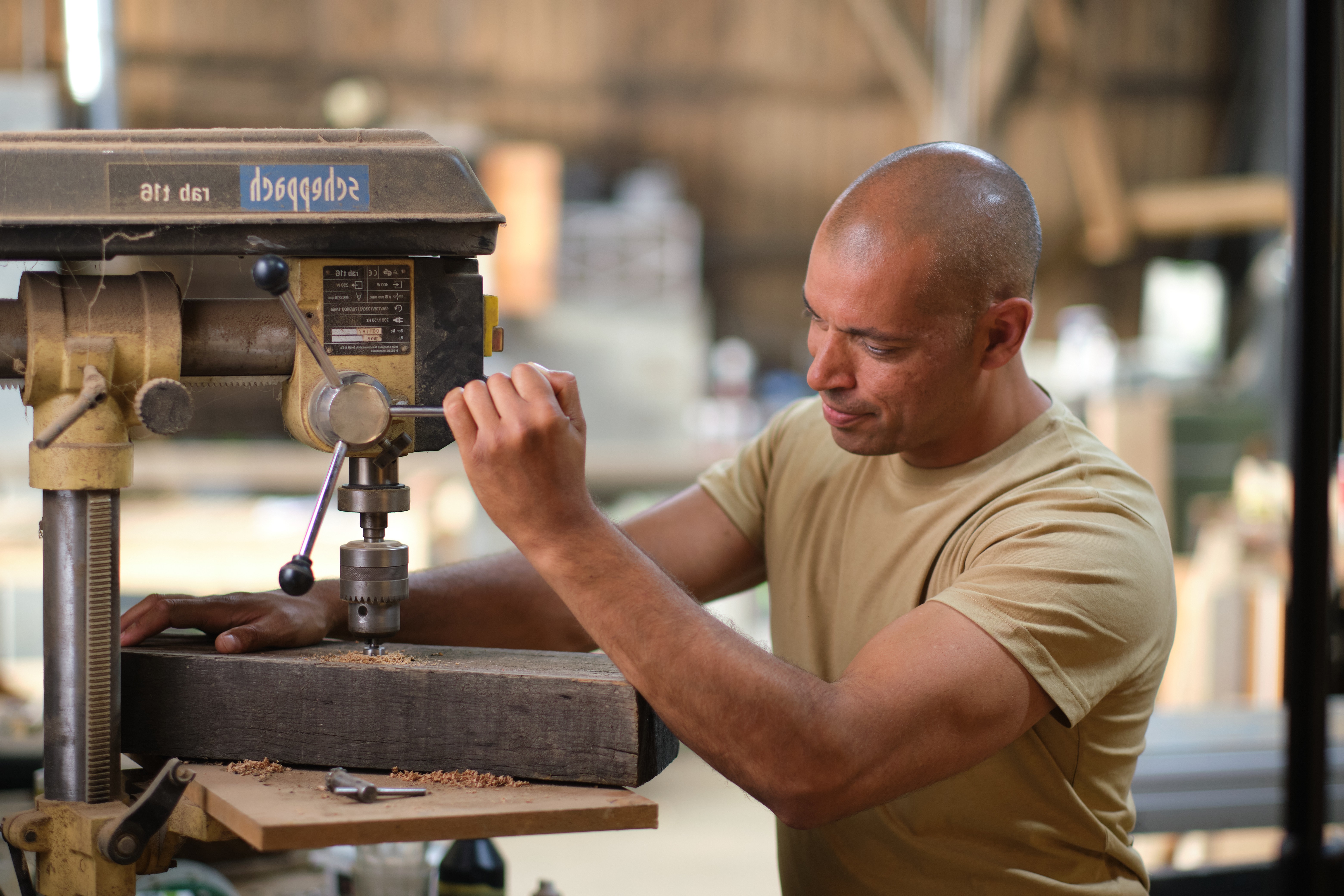    Een medewerker boort een gat in een houten balk met een kolomboormachine.