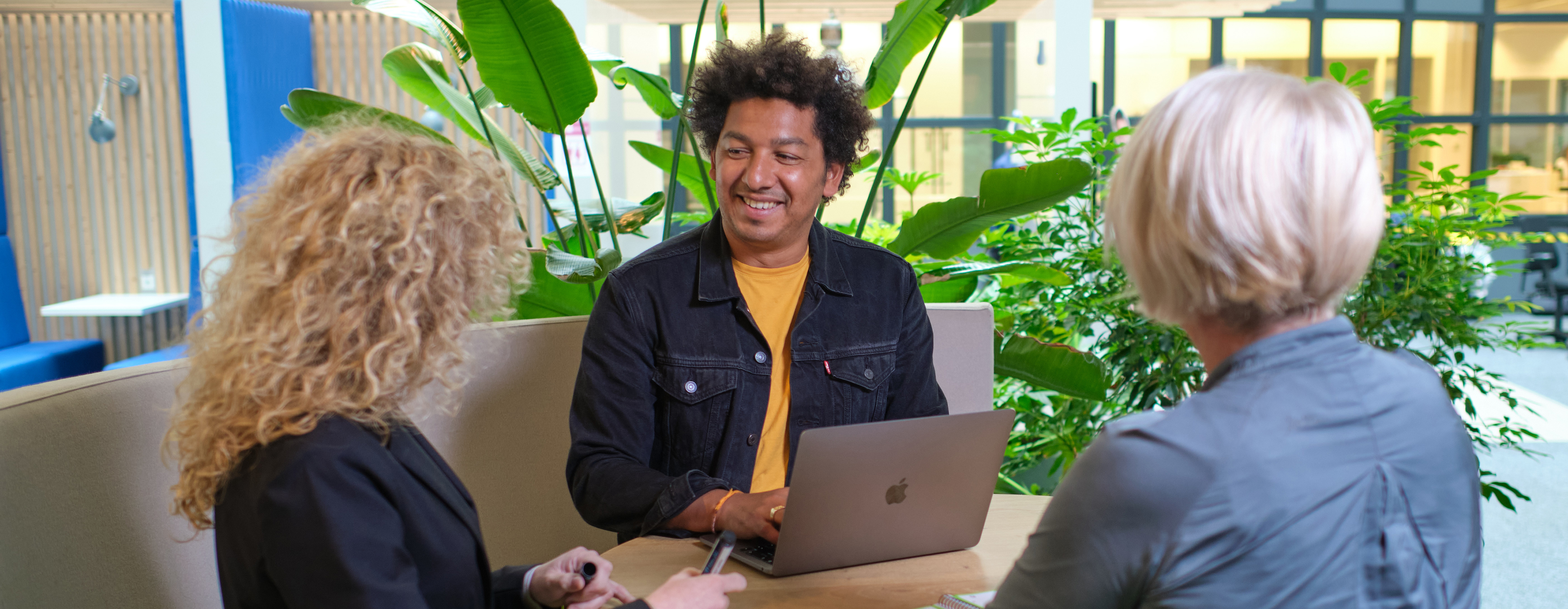 3 mensen zitten om de tafel. 1 man heeft een laptop