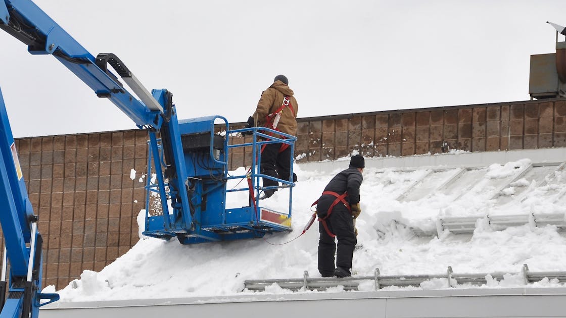 Twee mannen ruimen sneeuw van het dak