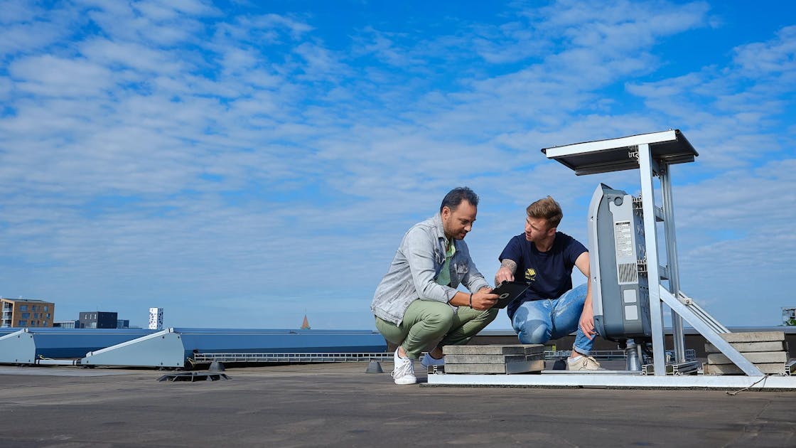 2 mannen op het dak kijken naar een tablet voor de installatie van zonnepanelen
